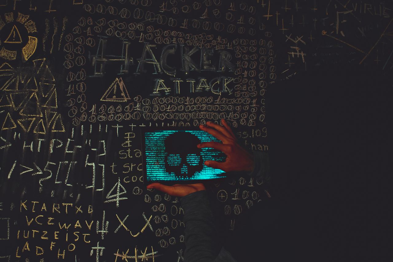 A hacker in a black hoodie using a tablet displaying a skull, surrounded by chalk symbols and 'Hacker Attack' text.